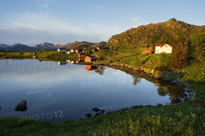 Landscape on the Lofoten Islands near Eggum. Houses on a fjord. At night at the time of the midnight sun in good weather, blue sky. Golden hour. Reflection. Early summer. Vestvagoya, Lofoten, Norway, Europe