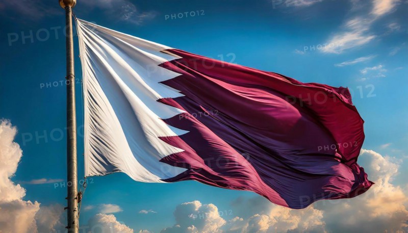 The flag of Qatar flutters in the wind, isolated against a blue sky