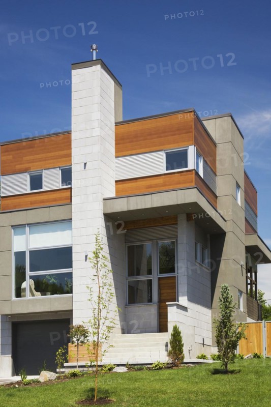Two story grey and charcoal stone with cedar wood siding modern cube style home facade in summer, Quebec, Canada, North America