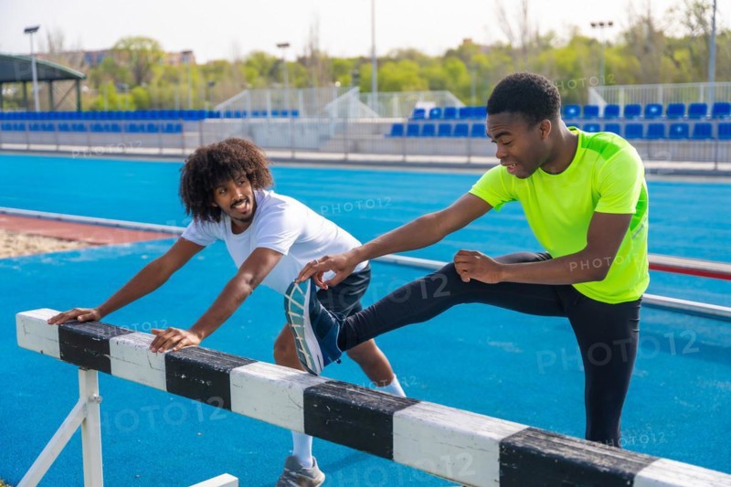 Two young african american sportsmen talking distracted while stretching legs in a running track