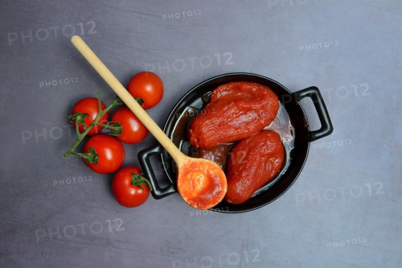 Whole tinned tomatoes in a pot, tomatoes and wooden spoon