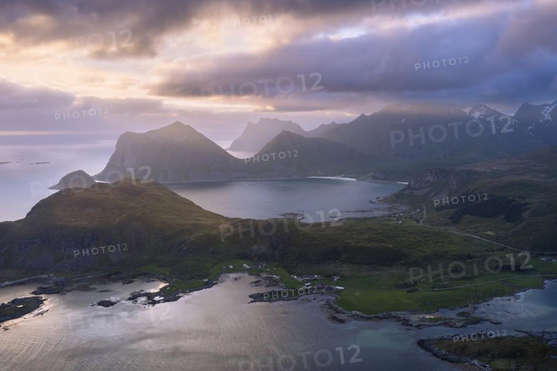 Landscape on the Lofoten Islands. View from the mountain Offersoykammen to the sea, the mountains Veggen, Mannen, Himmeltindan and Hogskolmen as well as the beaches of Haukland (Hauklandstranda) and Vik (Vik Beach) . At night at the time of the midnight sun. Clouds in the sky, sunlight from the side. Vestvagoya, Lofoten, Norway, Europe