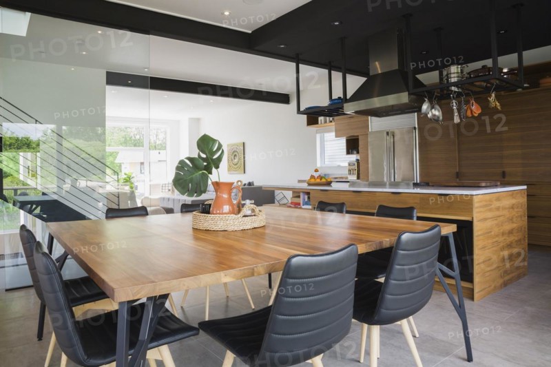 American walnut wood dining table and black leather sitting chairs with ash wood legs in dining room kitchen area inside modern cube style home, Quebec, Canada, North America