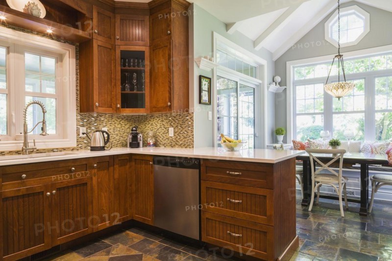 Kitchen with cherry wood cabinets, earth tone slate flooring and wooden breakfast table with sitting bench and rustic chairs inside a contemporary cottage style home, Quebec, Canada, North America