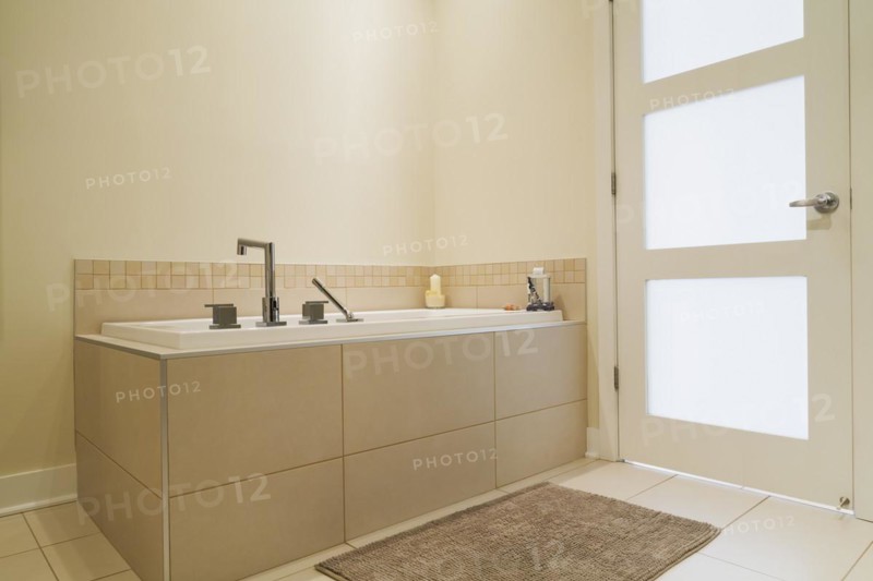 Soaking tub encased in a ceramic tile base in bathroom inside a renovated ground floor apartment in an old residential cottage style home, Quebec, Canada, North America