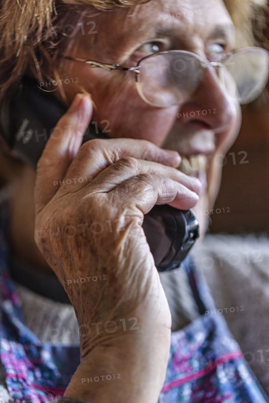 Laughing senior citizen with smock talking on the phone at home in her living room, Cologne, North Rhine-Westphalia, Germany, Europe