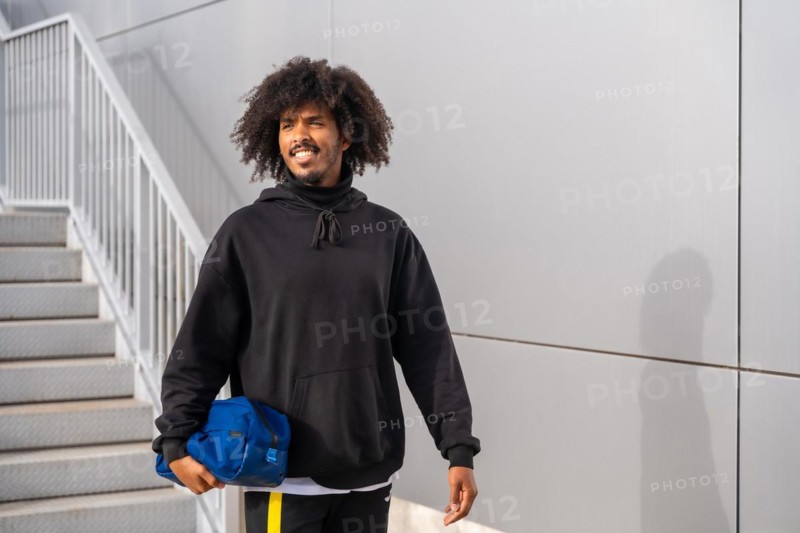 Sportive man with afro hairstyle walking next to stairs entering to a tennis court