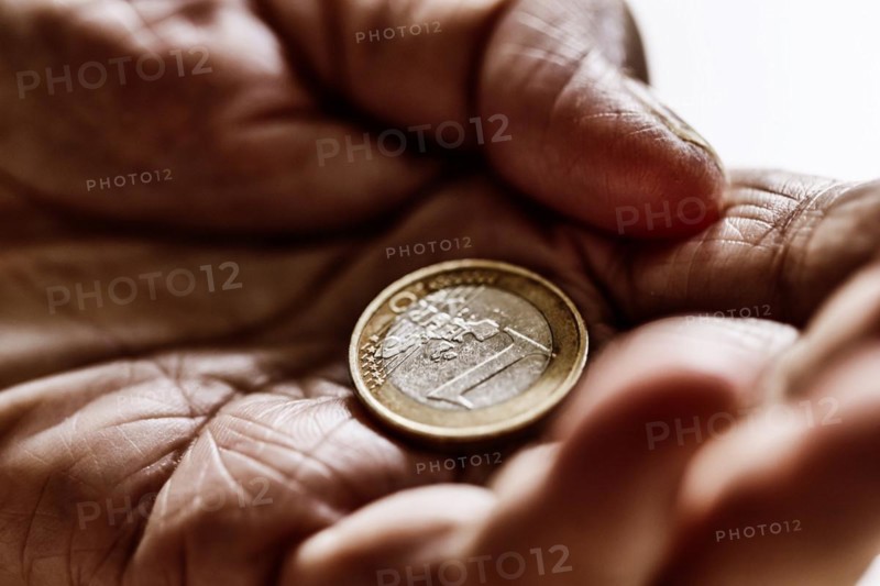 Euro coin in the wrinkled hand of a senior citizen, symbolising poverty and poverty in old age