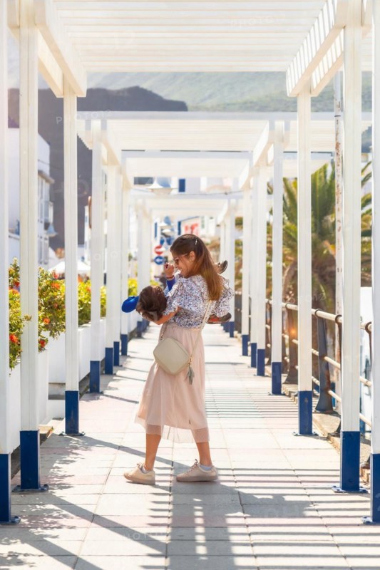 A woman is holding a child in a white building. The child is wearing a blue shirt
