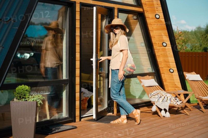 Mid-adult woman with string bag with vegetables on the porch of her log cabin