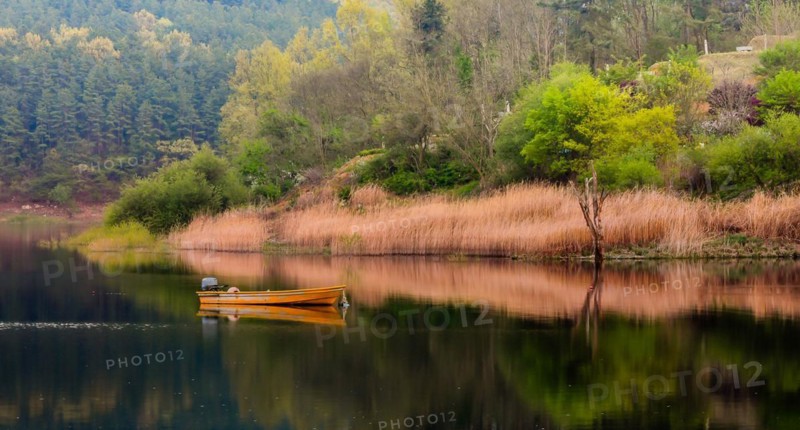 Small yellow metal fishing boat with small engine mount floating peacefully on a lake in South Korea