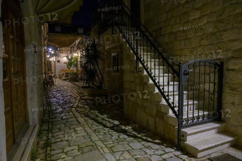 A narrow alley illuminated at night with alleyway lamp and outdoor seating of a restaurant, Trogir, Dalmatia, Croatia, Europe