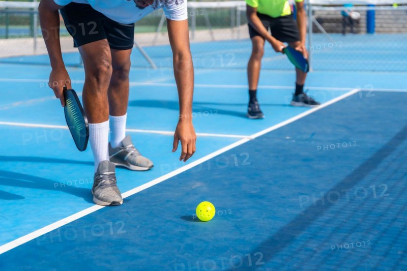 Cropped photo of the lower part of an african man bending to catch a pickleball ball from the floor in a court