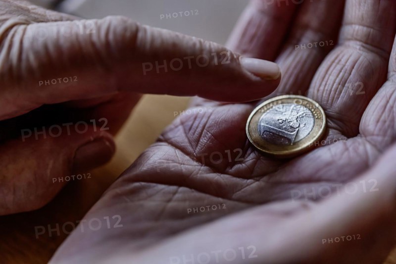 A euro coin in the wrinkled hand of a senior citizen, symbolising poverty and poverty in old age