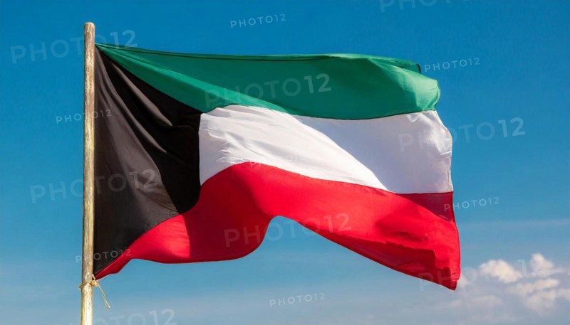 The flag of Kuwait flutters in the wind, isolated against a blue sky