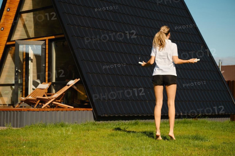 Mid adult a woman jumps with a smart rope on the lawn in front of tiny house