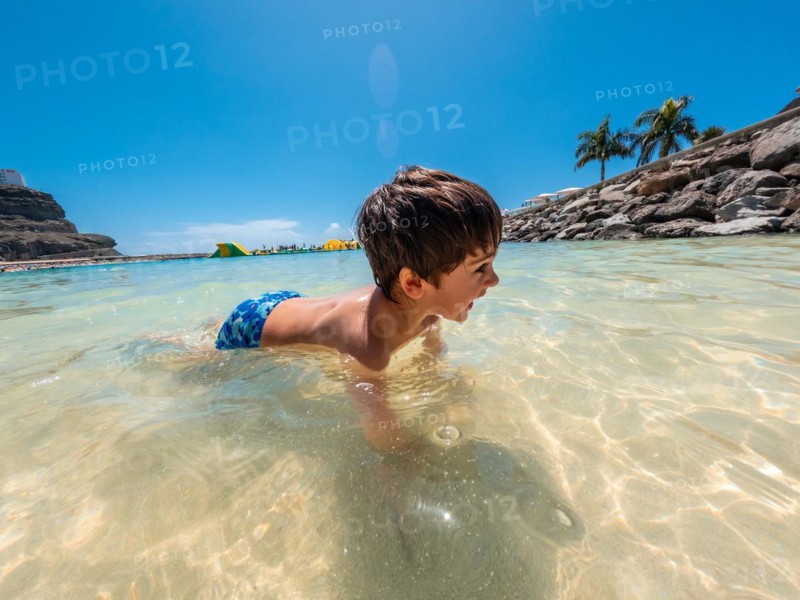 A young boy is swimming in the ocean. The water is clear and calm. The boy is wearing a blue swimsuit