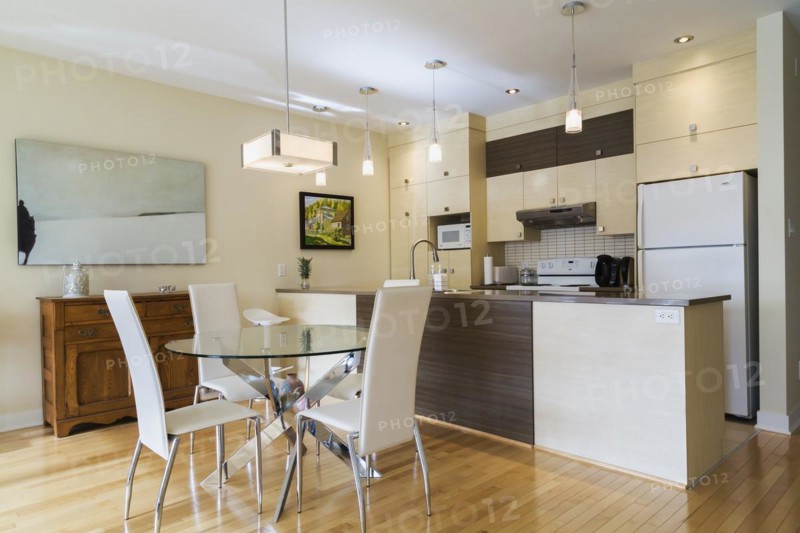 Dining room with round glass table, white leather high -back chairs and kitchen inside a renovated ground floor apartment in an old residential cottage style home, Quebec, Canada, North America