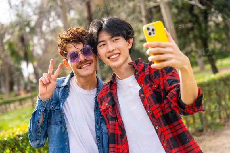 Young multiracial gay couple gesturing peace and talking selfie in a park