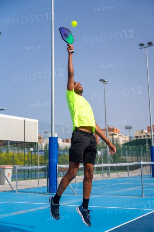 Vertical photo of a young african sportive man jumping playing pickleball outdoors