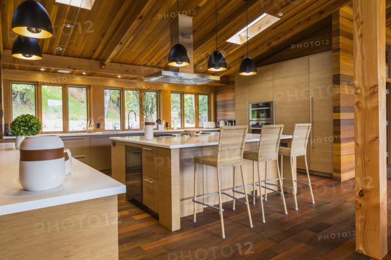 Bamboo wood buffet and island with white quartz countertops and high wicker chairs, cabinets in kitchen with Ipe wood floor plus black industrial style pendant lighting fixtures inside luxurious stained cedar and timber wood home with panoramic windows, Quebec, Canada, North America
