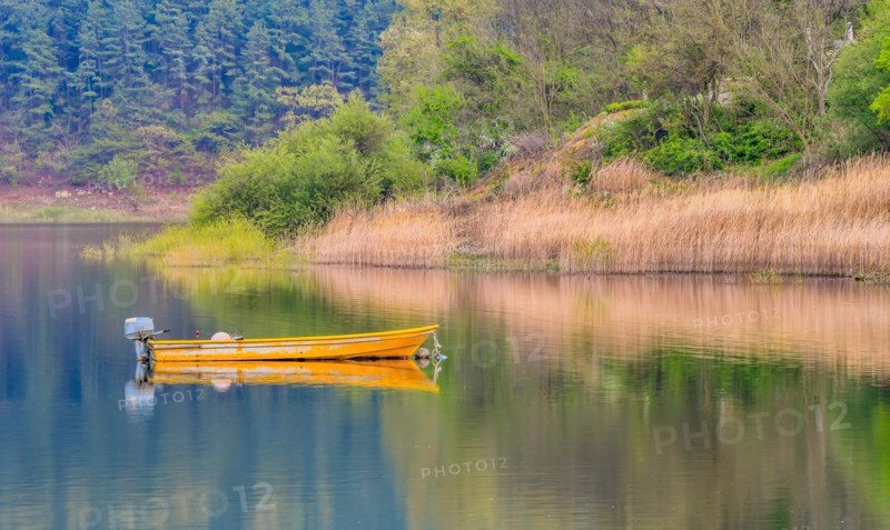 Small yellow metal fishing boat with small engine mount floating peacefully on a lake in South Korea