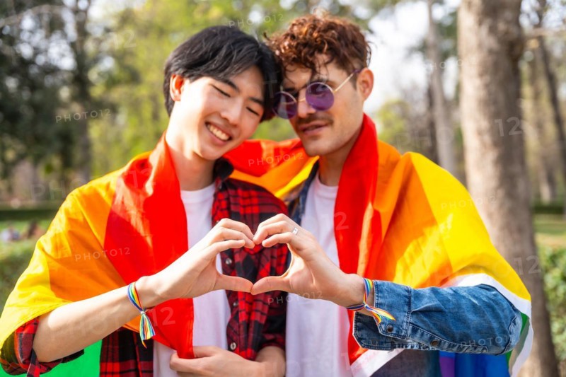 Multi-ethnic gay couple joining hands to form heart shape standing in a park