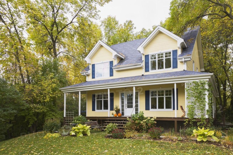 Two storey yellow clapboard with blue and white trim cottage style home facade in autumn, Quebec, Canada, North America