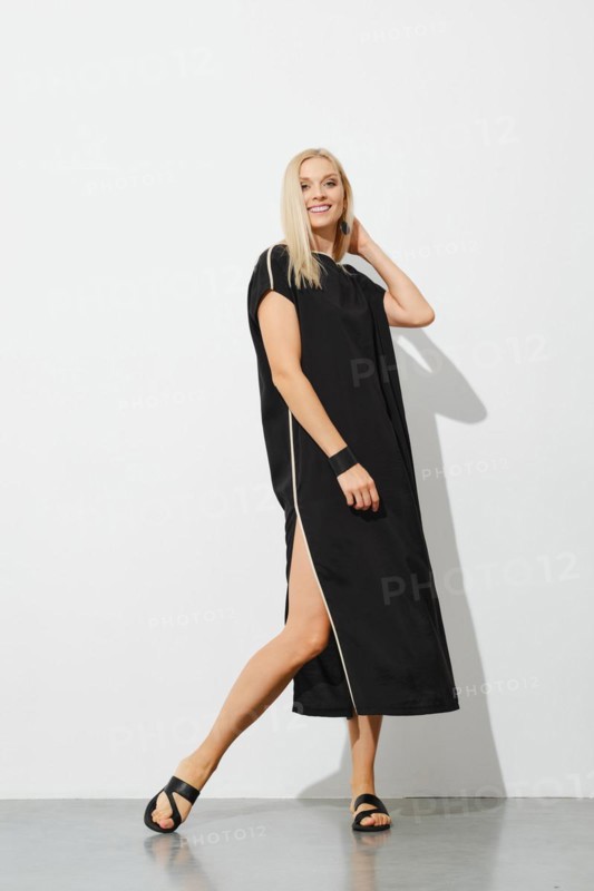 Beautiful blonde in black sleeveless dress posing next to white wall