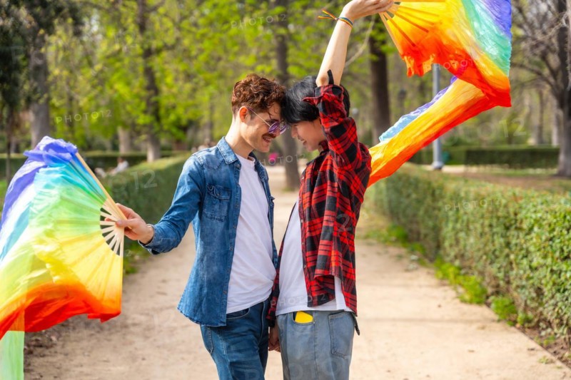 Side view of a multi-ethnic gay couple dancing using rainbow fans