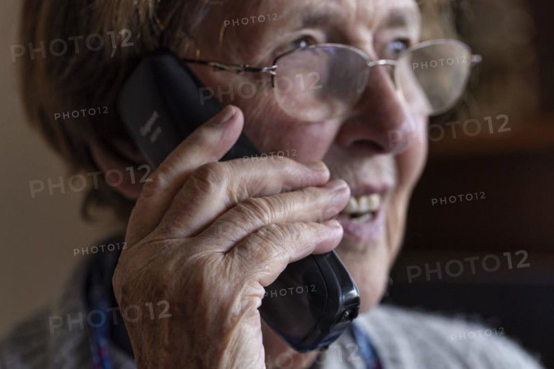 Laughing senior citizen with smock talking on the phone at home in her living room, Cologne, North Rhine-Westphalia, Germany, Europe
