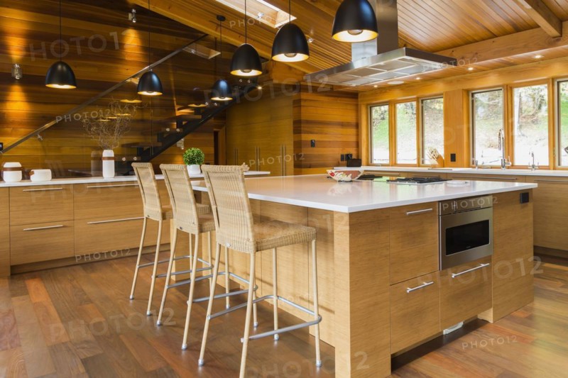 Bamboo wood island with white quartz countertops and high wicker chairs, buffet in kitchen with Ipe wood floor plus black industrial style pendant lighting fixtures inside luxurious stained cedar wood and timber home with panoramic windows, Quebec, Canada, North America