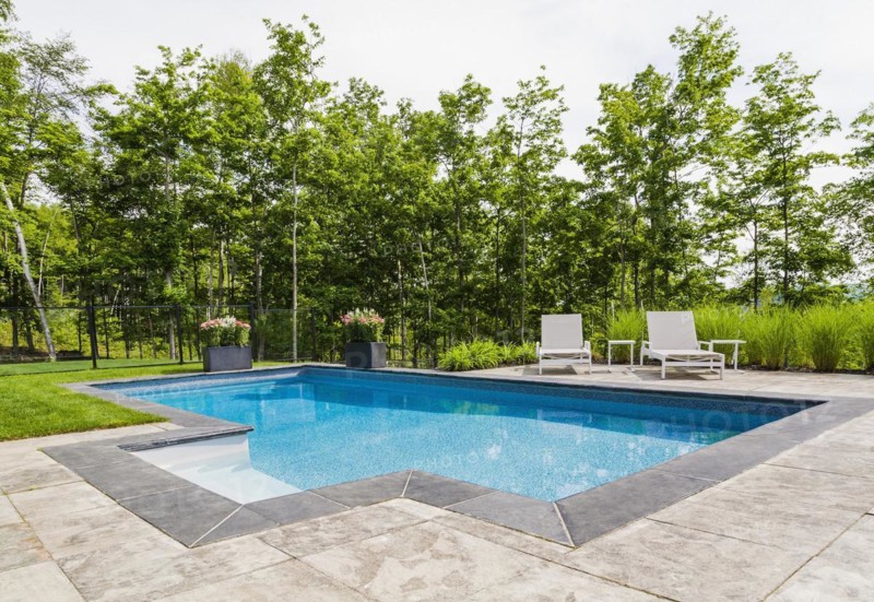 Two white long chairs on edge of in-ground swimming pool with flowers in planters in residential backyard in summer, Quebec, Canada, North America