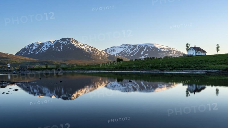 Landscape in Norway. The Balsfjord with a view of mountains and a house by the sea. At night at the time of the midnight sun, good weather, blue sky. Early summer. Reflection. Laksvatn, Troms, Norway, Europe