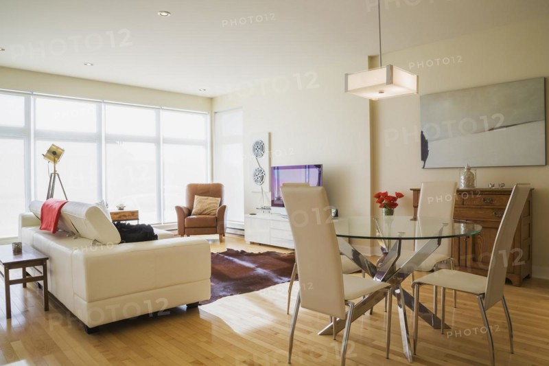 Dining room area with round glass table, white high-back leather chairs and white leather sofa in living room inside a renovated ground floor apartment in an old residential cottage style home, Quebec, Canada, North America