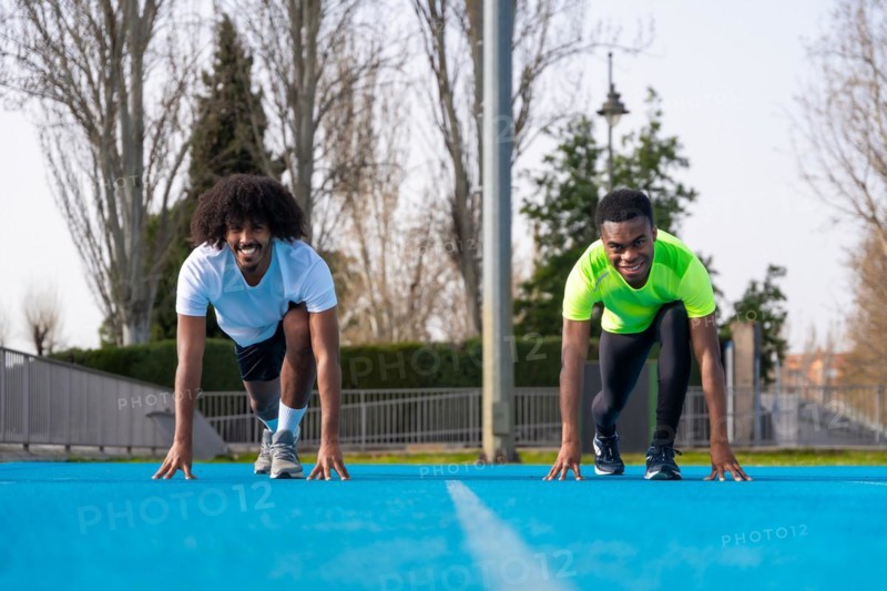 Frontal view of two sportive young african males in position to start a race in a blue running track