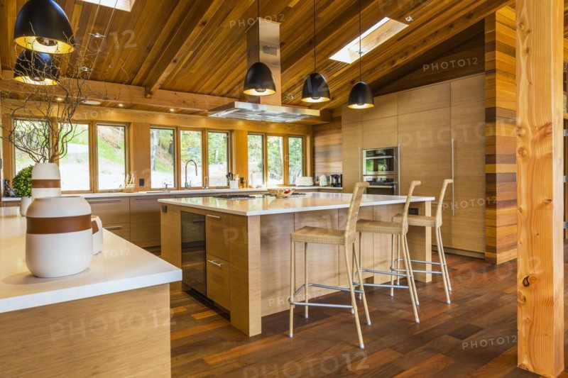 Bamboo wood buffet and island with white quartz countertops and high wicker chairs, cabinets in kitchen with Ipe wood floor plus black industrial style pendant lighting fixtures inside luxurious stained cedar and timber wood home with panoramic windows, Quebec, Canada, North America
