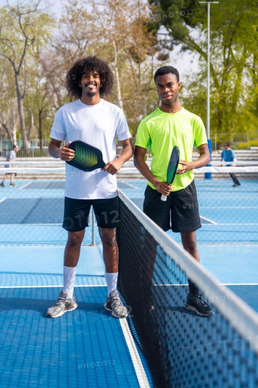 Vertical Portrait of two young african american pickleball players standing looking at camera holding pickleball equipment