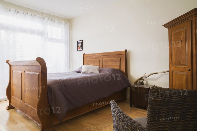 Antique wooden queen size sleigh bed in master bedroom inside a renovated ground floor apartment in an old residential cottage style home, Quebec, Canada, North America