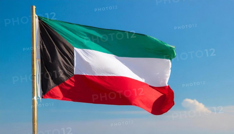 The flag of Kuwait flutters in the wind, isolated against a blue sky