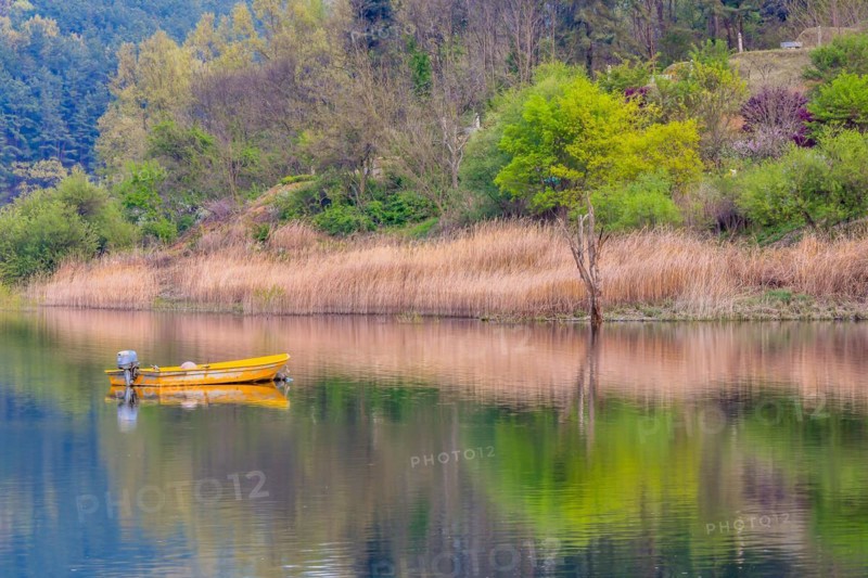 Small yellow metal fishing boat with small engine mount floating peacefully on a lake in South Korea