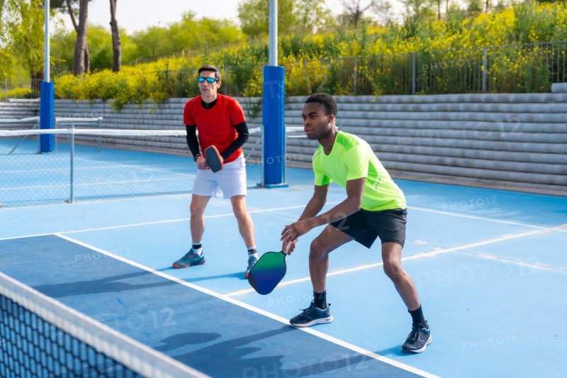 Full length photo of a multiracial team of pickleball players in an outdoor court in a sunny day