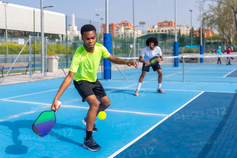 African young friends playing pickleball in an outdoor court in a sunny day