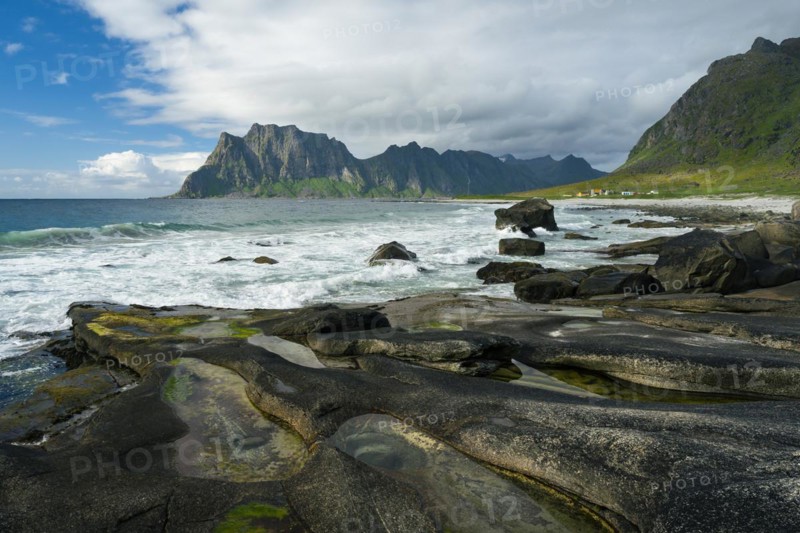 Seascape on the beach at Uttakleiv (Utakleiv), in the foreground rocks and rocky outcrops filled with water, including the so-called Eye of Uttakleiv, a round stone in the water. Mount Hogskolmen in the background. Sun and clouds. Early summer. Uttakleiv, Vestvagoya, Lofoten, Norway, Europe