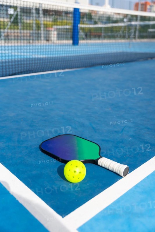 Vertical photo with copy space of a racket and yellow pickleball ball on a court