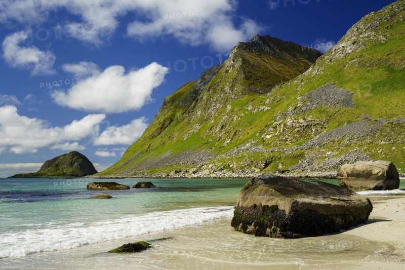 Landscape with sea at the sandy beach of Haukland (Hauklandstranda) with the mountain Veggen. Some rocks on the beach and in the sea. Blue sky, some clouds. Early summer. Haukland Beach, Haukland, Vestvagoya, Lofoten, Norway, Europe