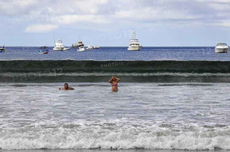 San Juan del Sur, Nicaragua, swimmers in the water in front of a big wave, boats and blue sky in the background, Central America, Central America