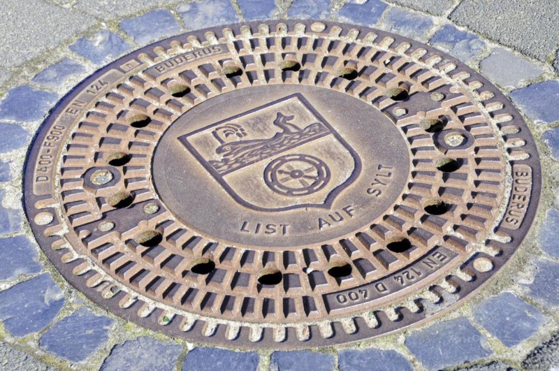 List, A manhole cover with engraved coat of arms and lettering, surrounded by paving stones, Sylt, North Frisian Island, Schleswig-Holstein, Germany, Europe