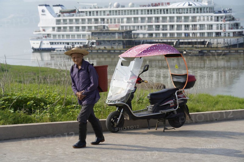 Cruise ship on the Yangtze River, A man walks next to an electric rickshaw, in the background a large cruise ship on the river, Yangtze River, Chongqing, Chongqing Province, China, Asia