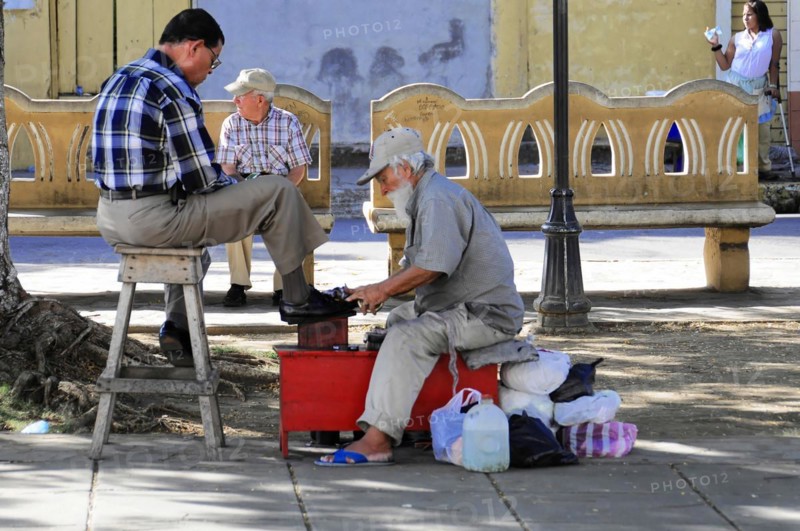 Leon, Nicaragua, A shoeshine boy serves a customer on the street under the shade of the trees, Central America, Central America
